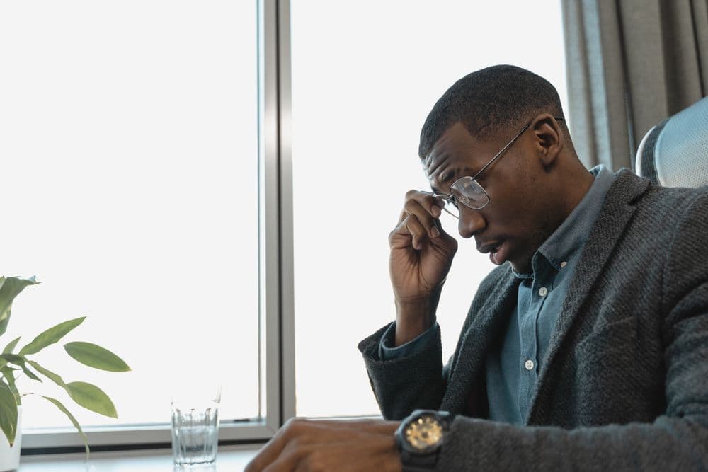 A man pausing at his desk and taking off his glasses