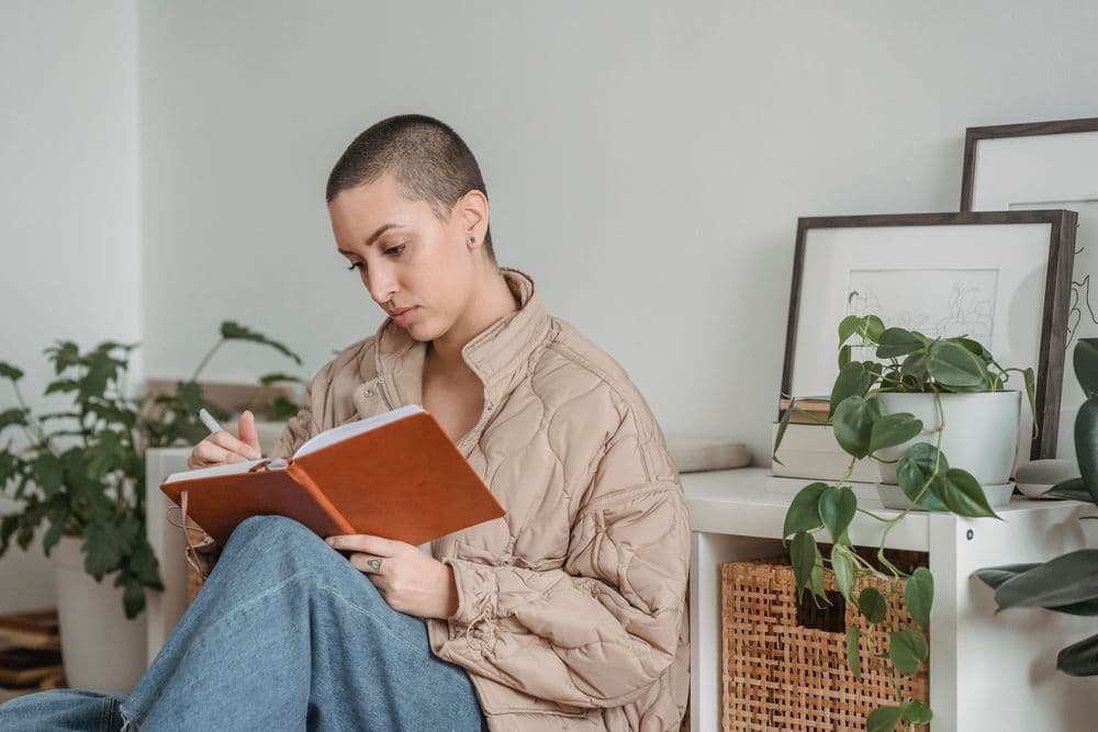 A woman writing in a notebook beside houseplants