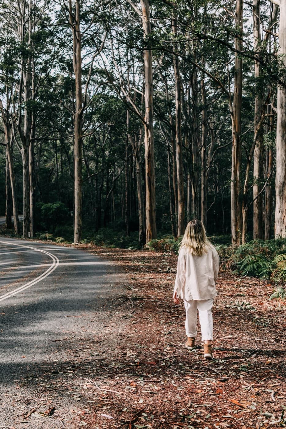 A woman walking along a quiet road through tall trees