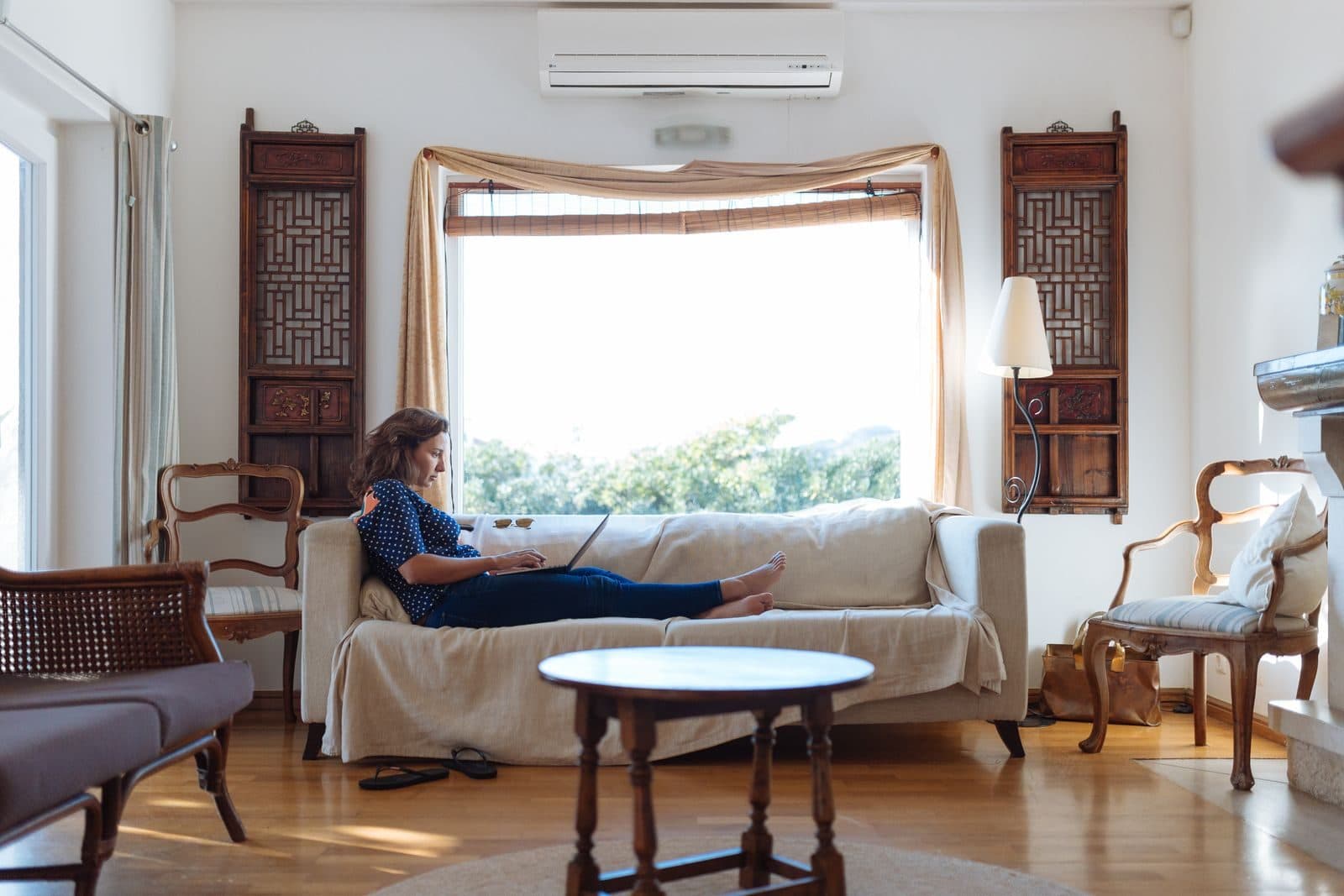 A woman resting on a sofa with a laptop in a bright living room
