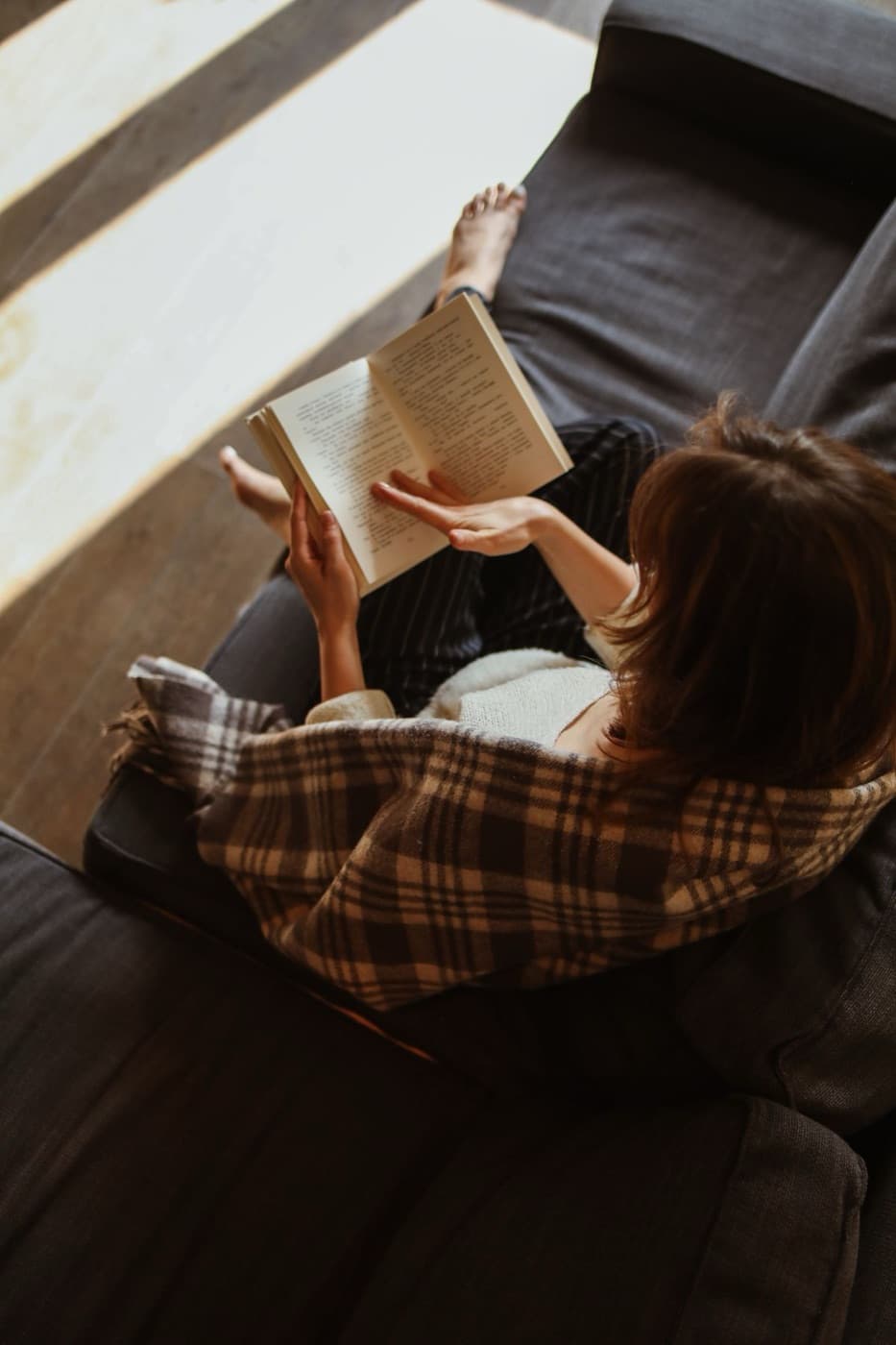 A woman reading on the sofa under a checked blanket