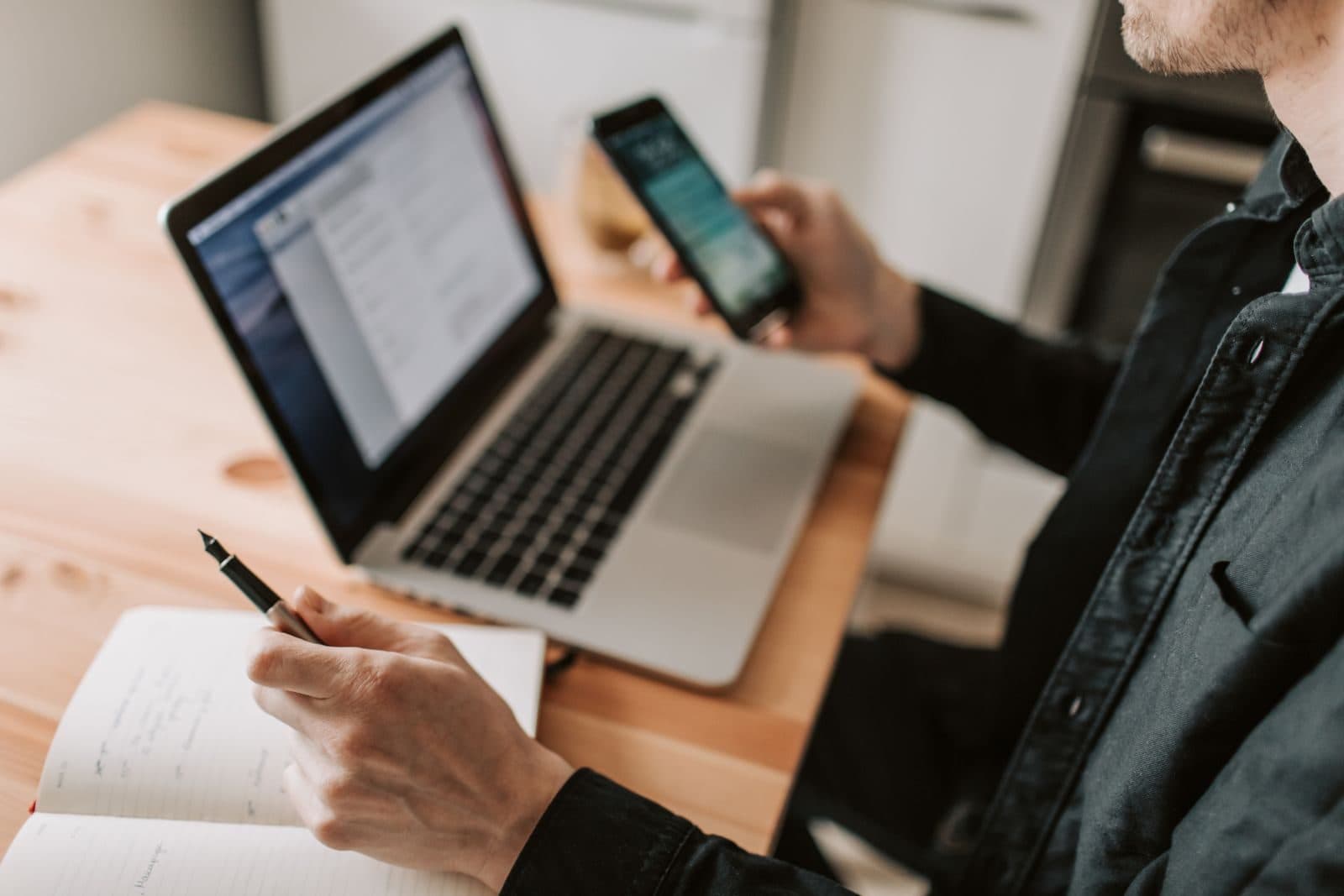 A man comparing options on his laptop and phone while taking notes