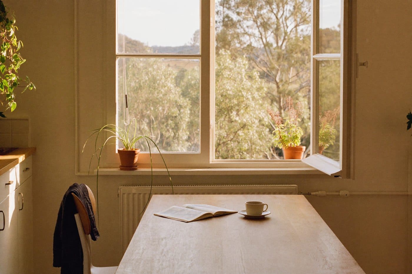 A sunlit kitchen table in the morning, journal and coffee by an open window