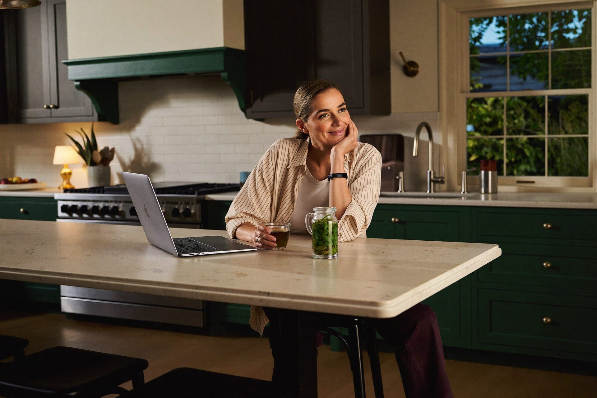 A woman at her kitchen bench in the evening, laptop open, finally calm