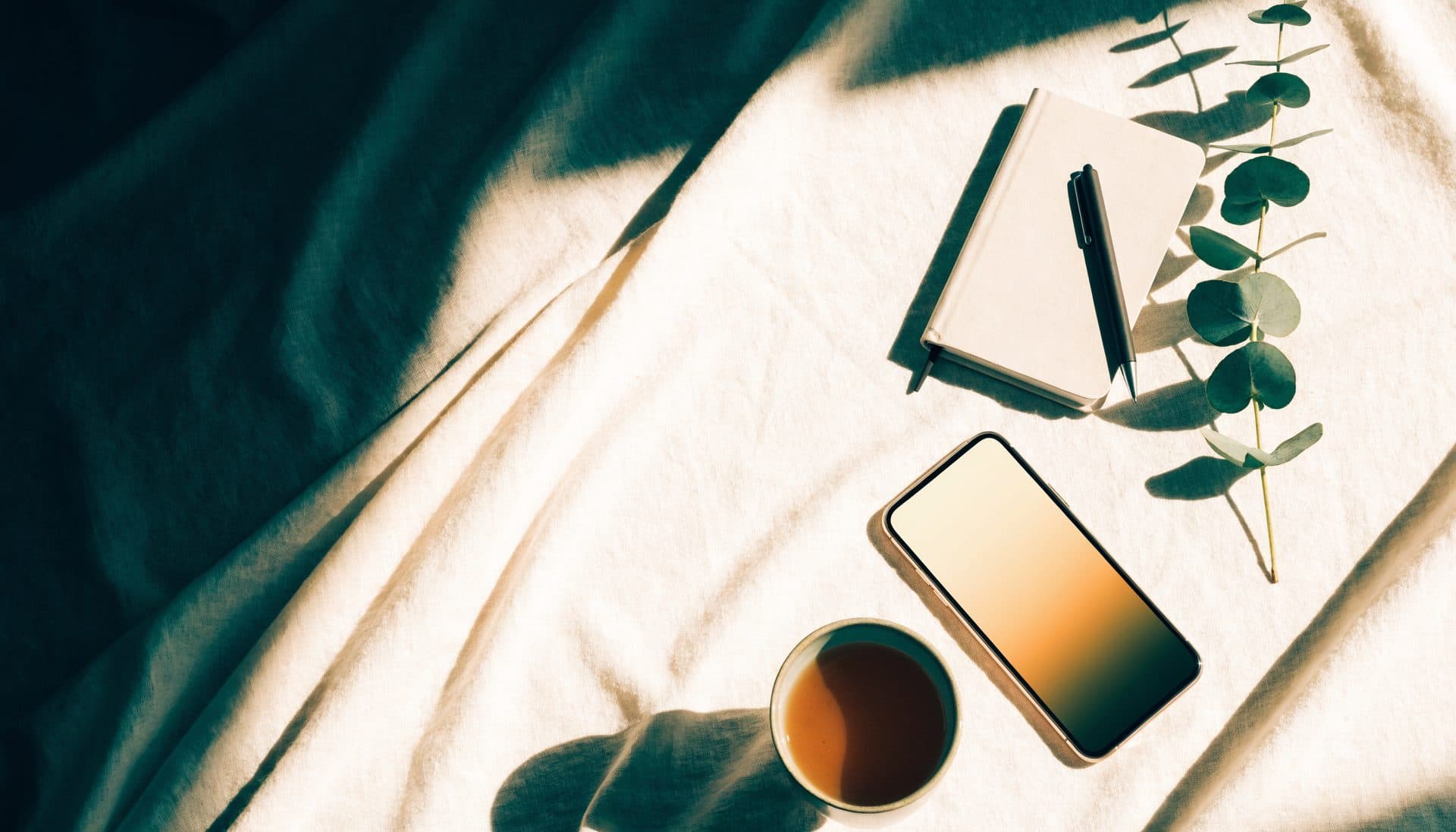 A cup of tea, phone and notebook laid out in calm morning light
